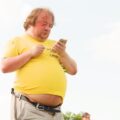 Fat American looking at his phone while crossing the street.